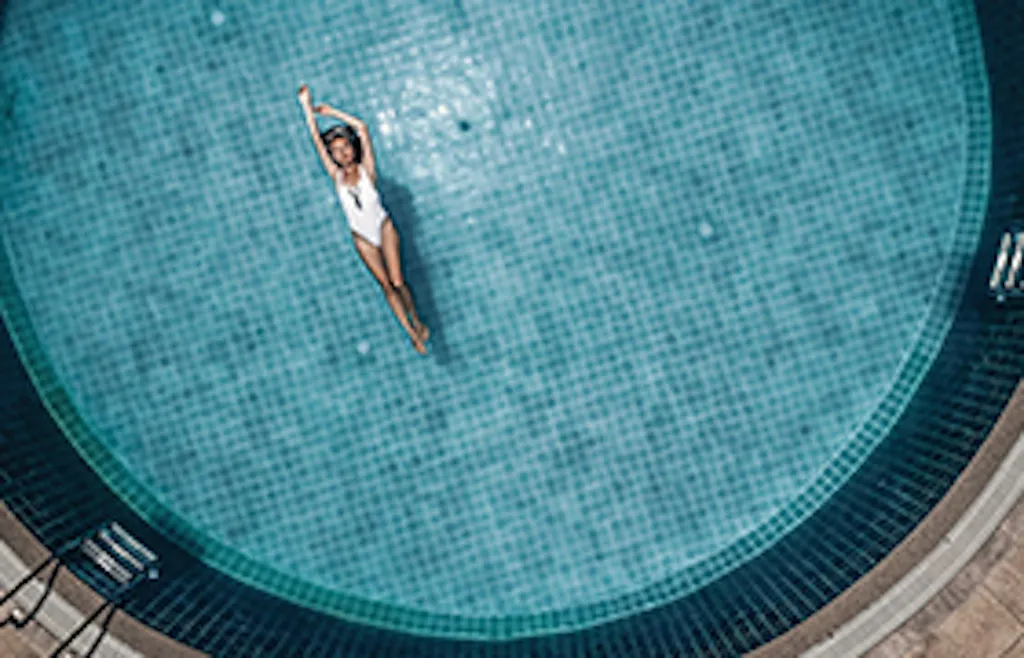 Une personne nage dans une piscine circulaire turquoise vue d'en haut.
