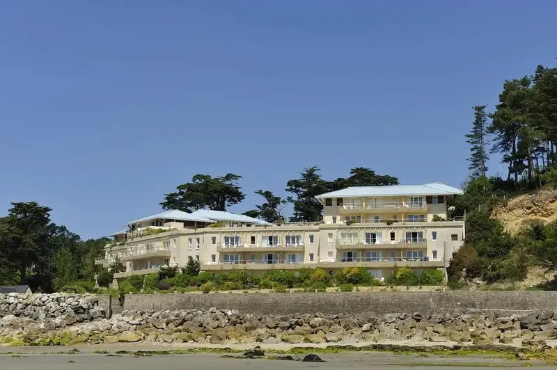Bâtiment beige avec des balcons donnant sur une plage de galets.