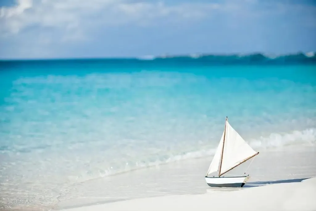 Un petit voilier blanc est échoué sur une plage de sable fin au bord d'une mer turquoise.