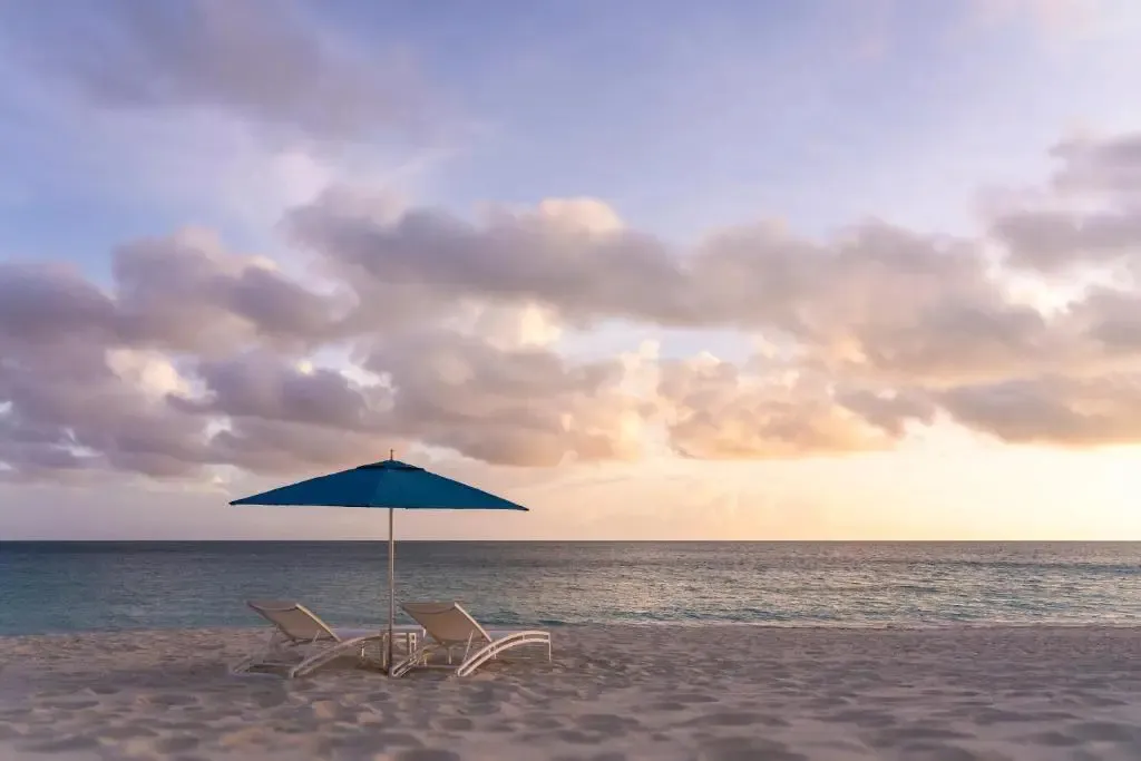 Deux transats bleus sont installés sur une plage de sable fin face à la mer au coucher du soleil.