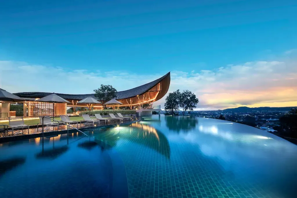 Une piscine à débordement offre une vue sur un paysage vallonné au coucher du soleil.