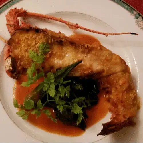 Un plat de homard grillé est servi avec une sauce et des légumes verts.