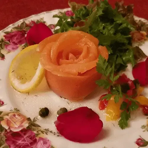 Assiette ornée d'une fleur de saumon, de citron, de salade et de pétales de rose.