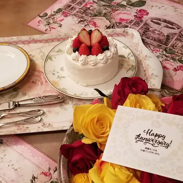 Une table dressée présente un gâteau décoré de fraises et un bouquet de roses multicolores.