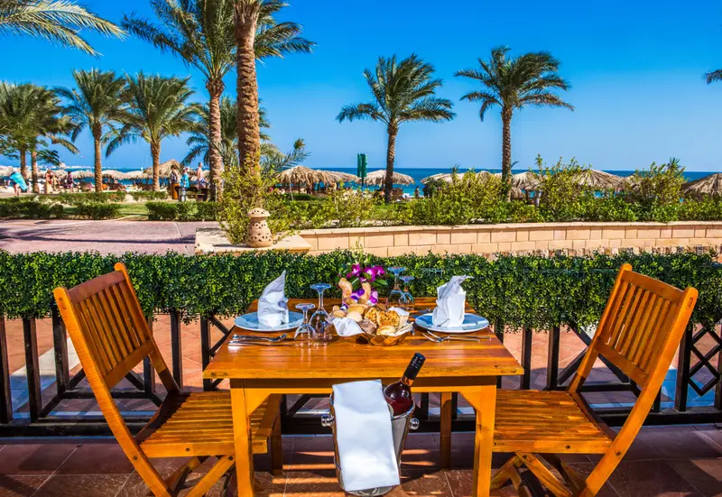 Une table dressée pour un repas en extérieur avec vue sur la mer et la végétation.