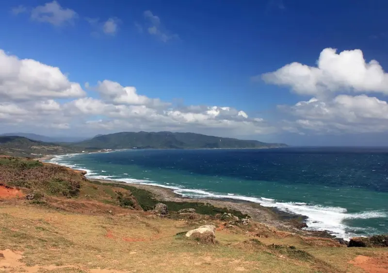 Vue panoramique sur une côte rocheuse et une mer turquoise sous un ciel nuageux.