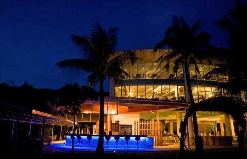 Un bar illuminé en bleu se trouve devant un bâtiment moderne avec de grandes fenêtres.