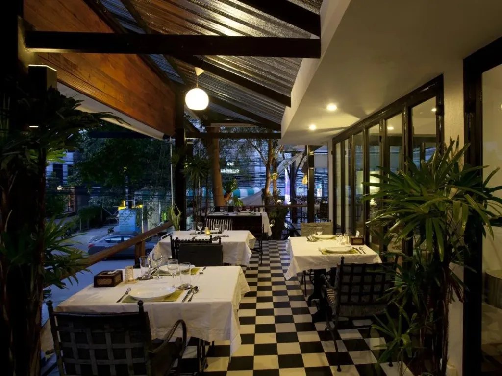 Une salle à manger extérieure avec des tables dressées et un sol à carreaux.