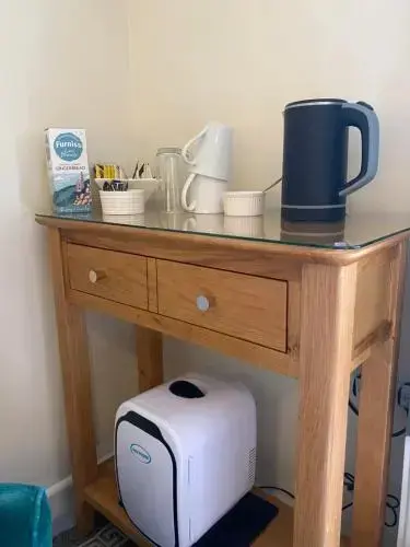 Une console en bois présente une bouilloire électrique, une cafetière et des accessoires pour le thé et le café.