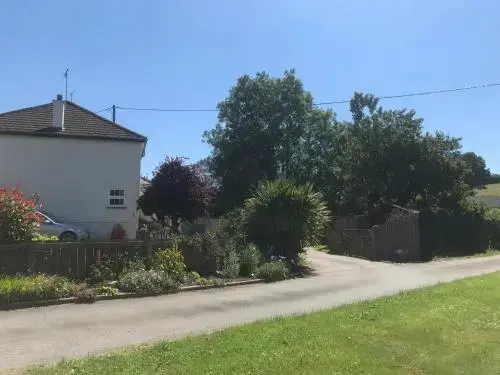 Bâtiment blanc à deux étages avec un jardin verdoyant et une route en contrebas.