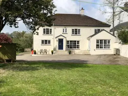 Maison blanche à deux étages avec un jardin verdoyant devant.