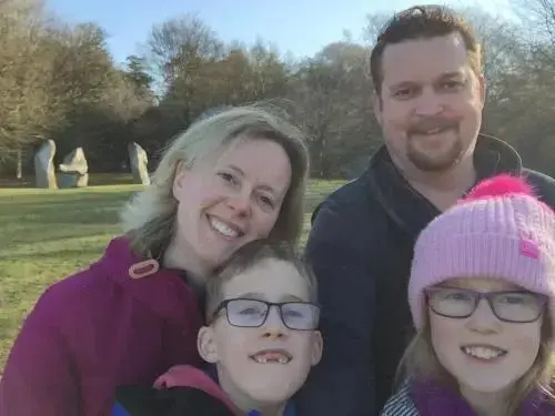 Portrait d'une famille souriante devant un paysage verdoyant et des pierres dressées.