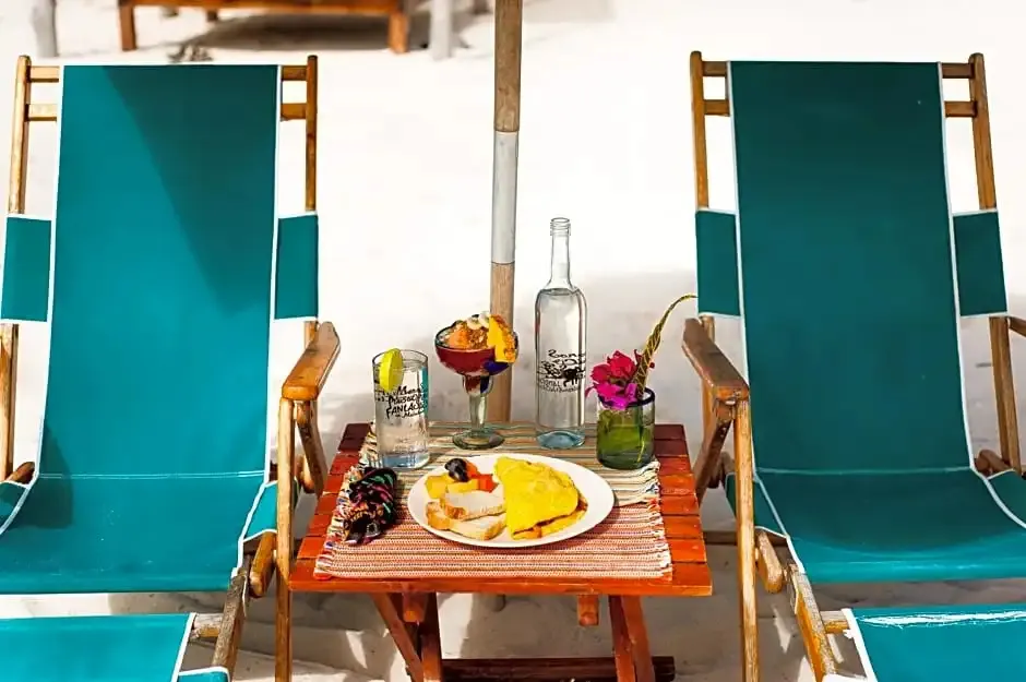 Deux transats verts sont disposés de part et d'autre d'une petite table en bois sur une plage de sable blanc.