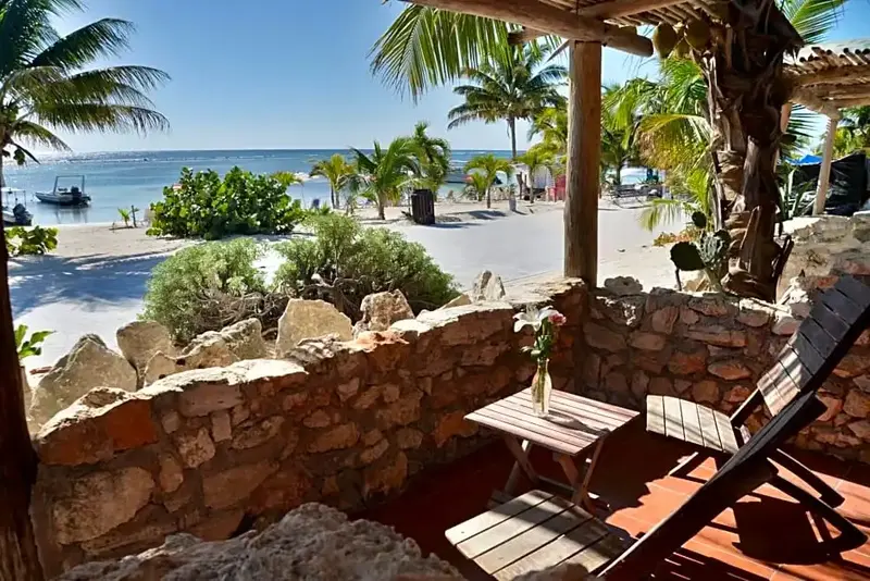 Terrasse en pierre avec mobilier de jardin donnant sur une plage de sable blanc et la mer.