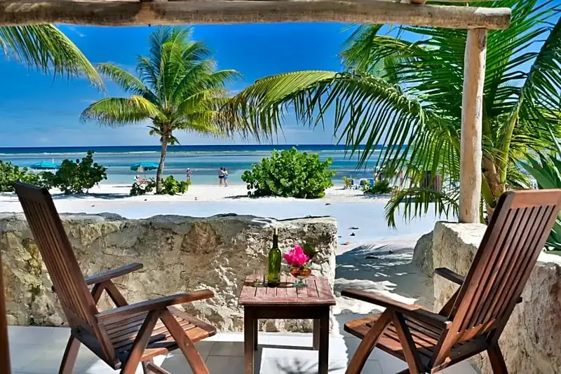 Deux fauteuils en bois donnent sur une plage de sable blanc bordée de palmiers.