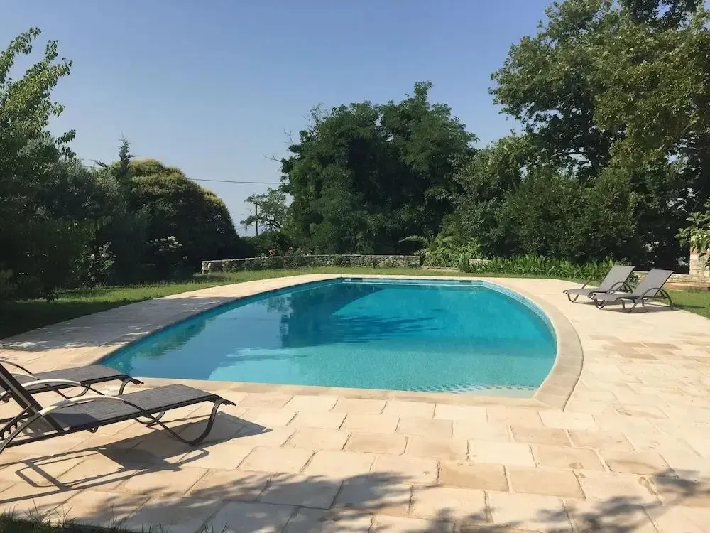 Piscine rectangulaire entourée d'une terrasse en pierre et de végétation luxuriante.