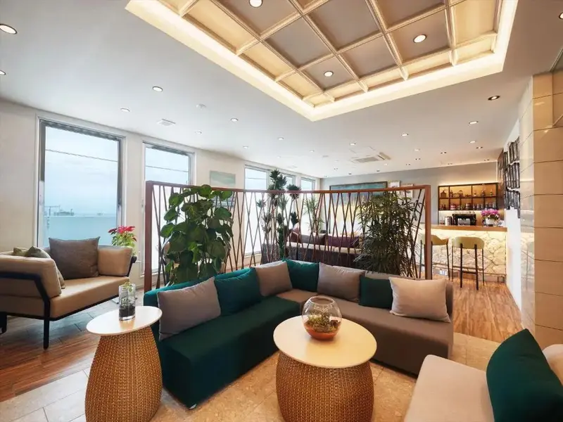 Espace de détente intérieur avec canapés et tables basses près de grandes fenêtres.