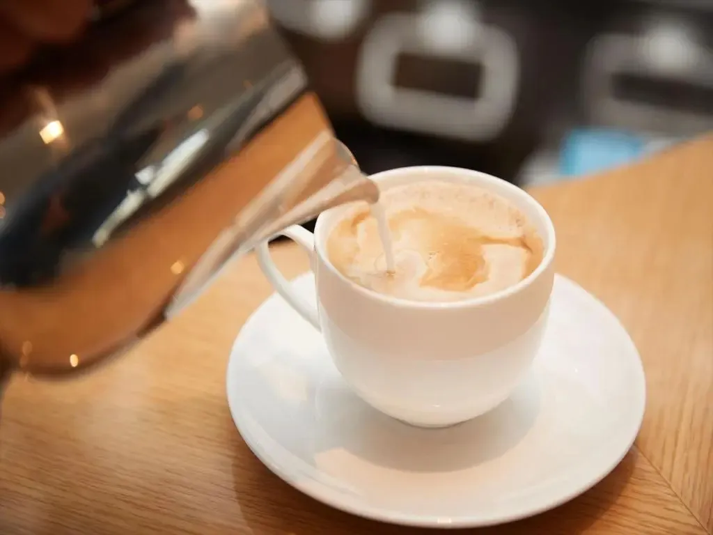 Un café au lait est versé dans une tasse blanche sur une soucoupe.