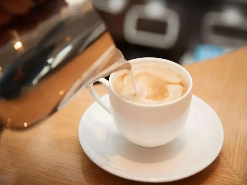 Un café au lait est versé dans une tasse blanche sur une soucoupe.