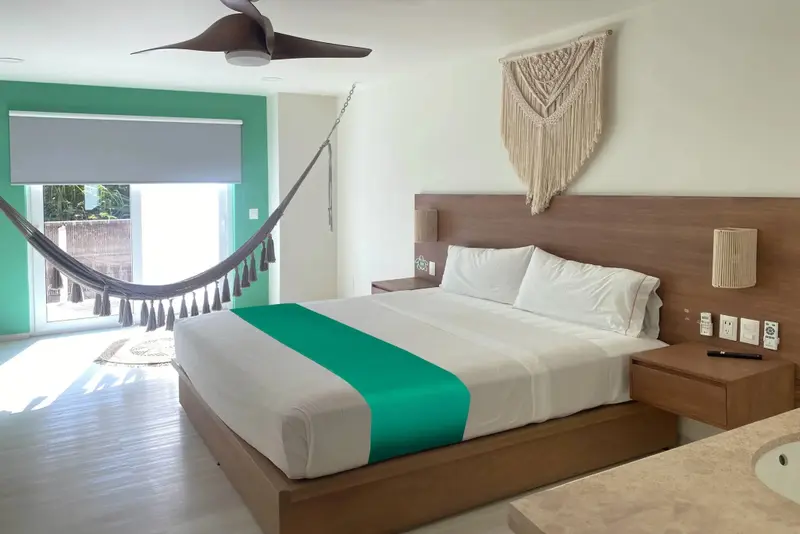 Une chambre lumineuse avec un grand lit et un hamac près de la fenêtre.