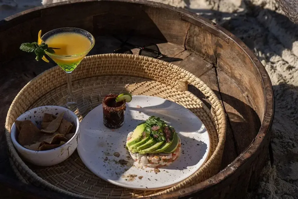 Assiette de ceviche et cocktail servis sur un plateau en osier.