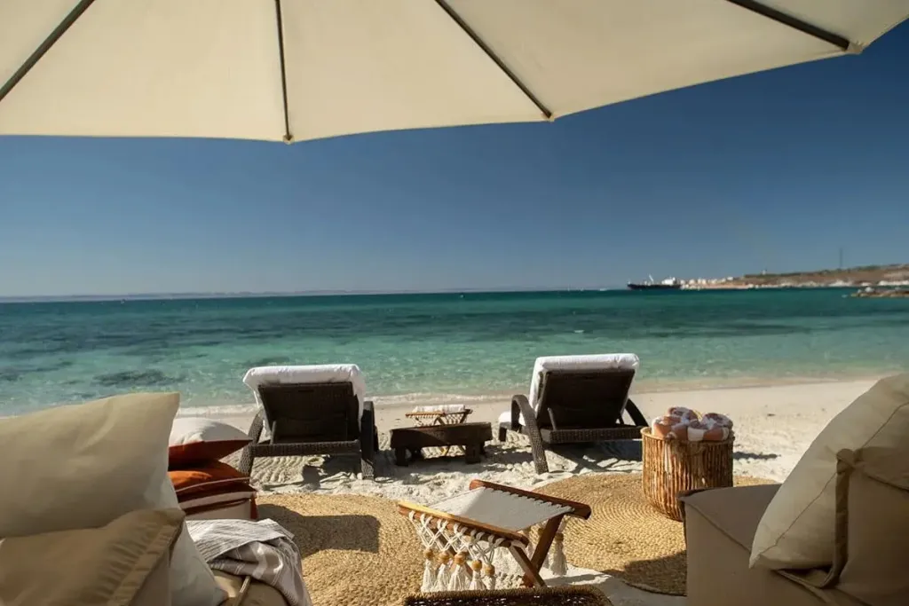 Deux transats blancs invitent à la détente sur une plage de sable fin face à la mer.