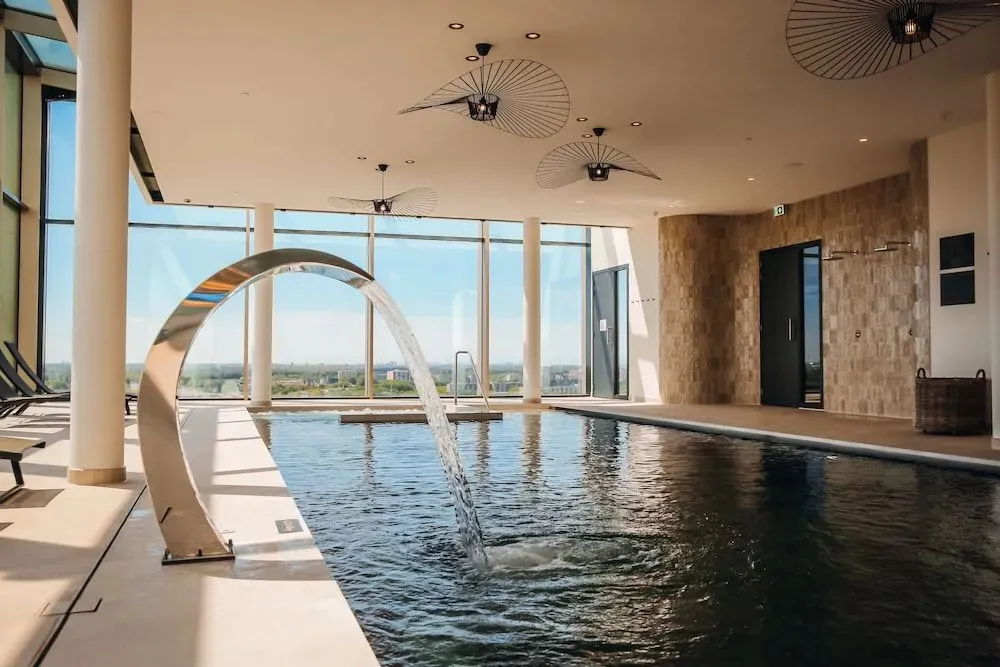Une piscine intérieure avec une cascade et une grande baie vitrée offrant une vue sur le paysage.