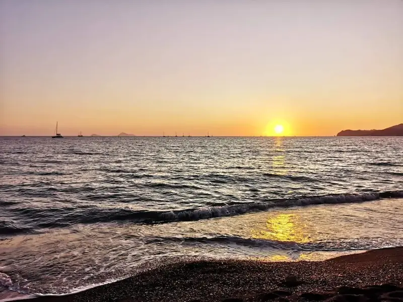 Le soleil se couche sur une mer calme avec une plage de galets au premier plan.
