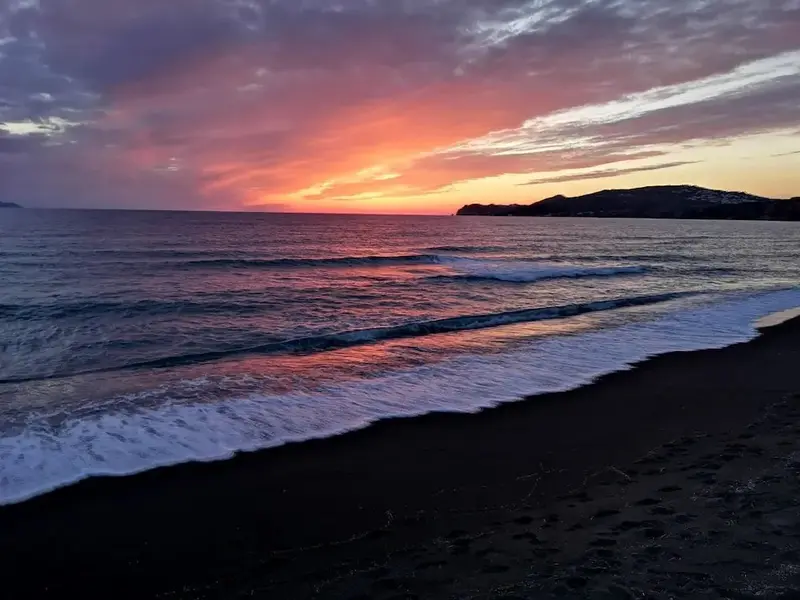 Coucher de soleil sur une plage de sable noir avec des vagues.