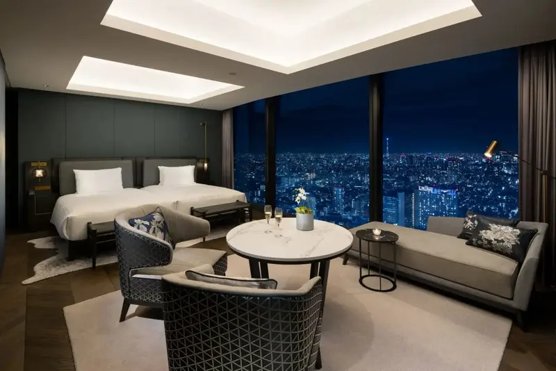 Une chambre moderne avec un grand lit et un coin salon offre une vue nocturne sur la ville.