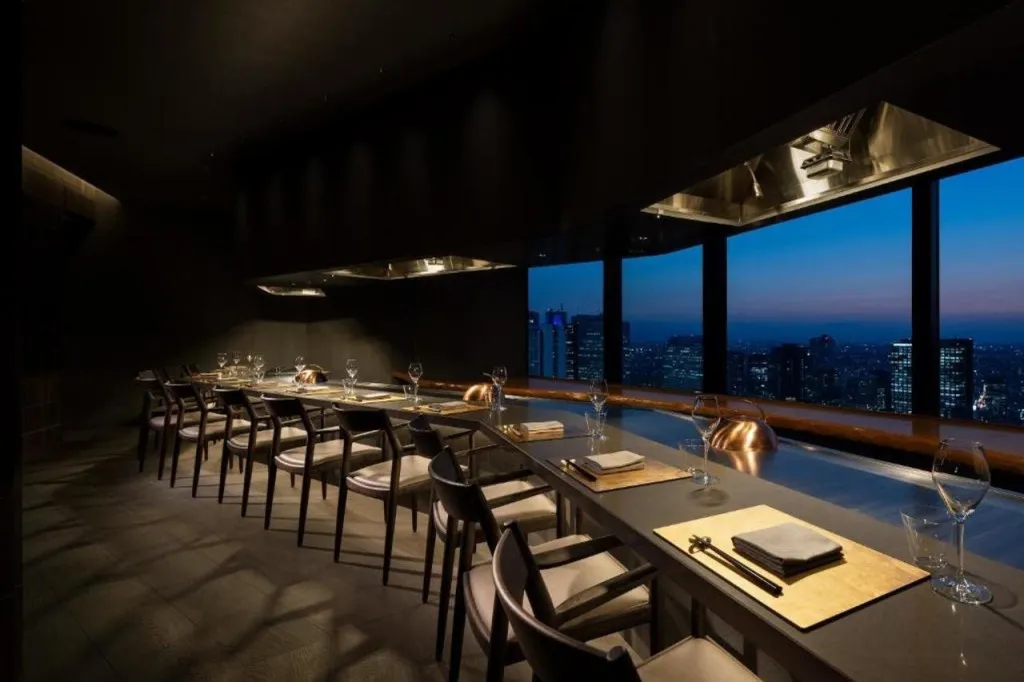 Une salle de restaurant élégante offre une vue panoramique sur une ville illuminée au crépuscule.