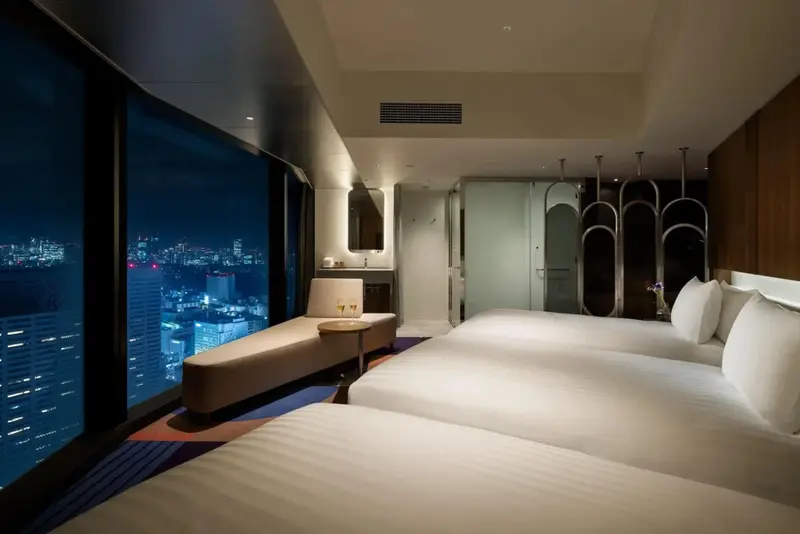 Une chambre d'hôtel moderne avec de grands lits et une vue nocturne sur la ville.