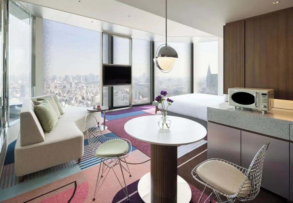 Espace de vie moderne avec canapé, table ronde et kitchenette donnant sur une vue urbaine.