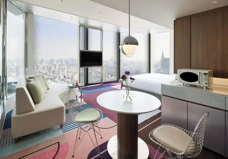 Espace de vie moderne avec canapé, table ronde et kitchenette donnant sur une vue urbaine.
