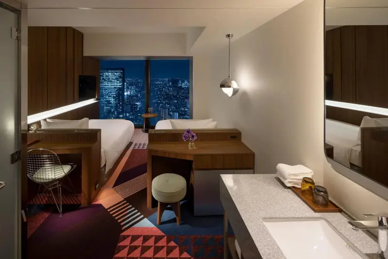 Une chambre moderne avec deux lits et une vue nocturne sur la ville.