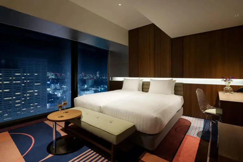 Une chambre moderne avec un grand lit face à une vue nocturne sur la ville.