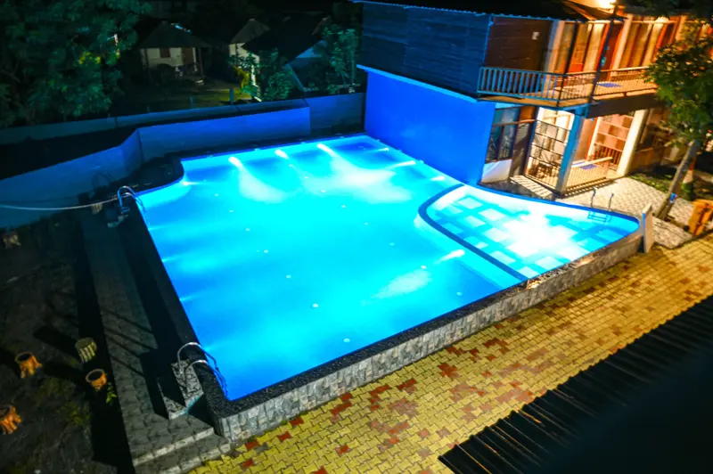 Piscine illuminée avec des escaliers et un bâtiment éclairé en arrière-plan.