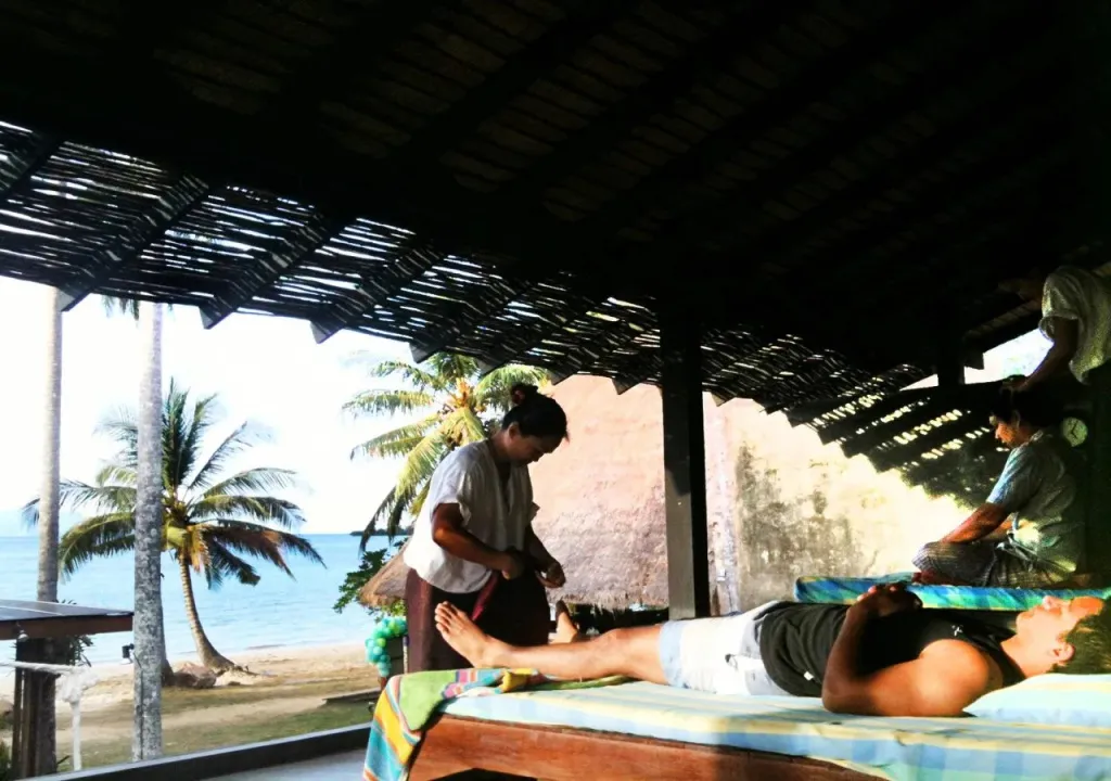 Deux personnes reçoivent un massage en bord de mer sous une structure ajourée.