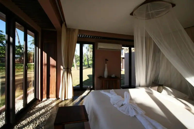 Une chambre lumineuse s'ouvre sur un jardin tropical par de grandes baies vitrées.
