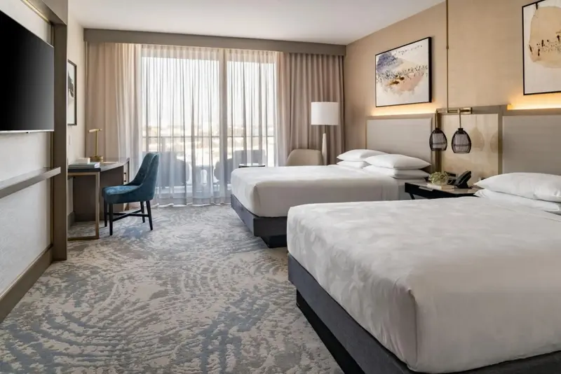 Une chambre lumineuse avec deux lits et un bureau près d'une fenêtre.