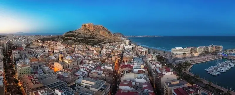 Vue panoramique d'une ville côtière avec une colline rocheuse et un port de plaisance.