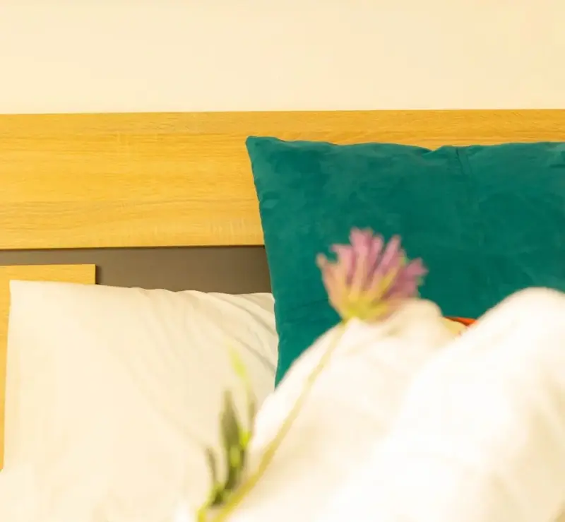 Un lit avec des oreillers blancs et un coussin vert turquoise est prêt pour le repos.