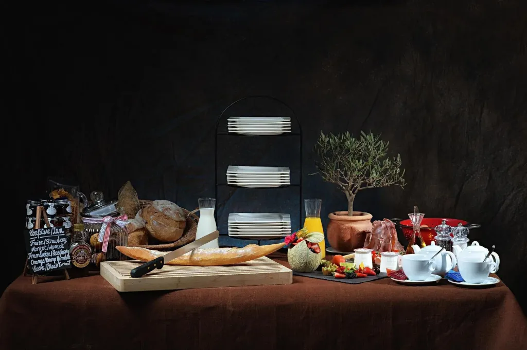 Nature morte gourmande avec viennoiseries, fruits et couverts sur une table recouverte d'une nappe.