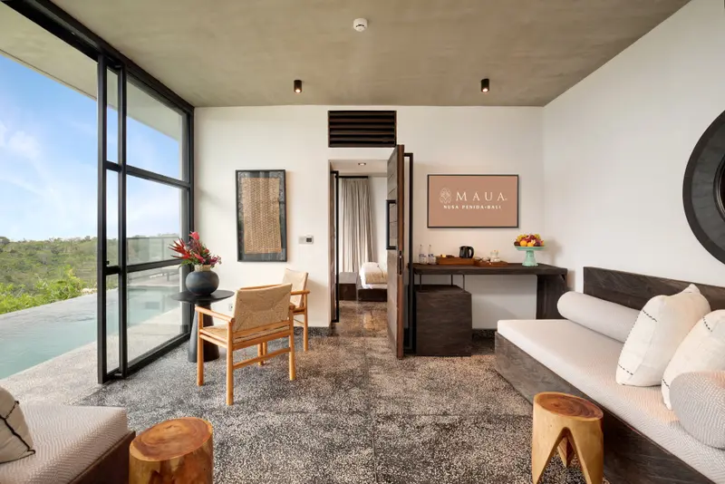 Espace de vie intérieur lumineux avec canapé, fauteuil et vue sur l'extérieur.