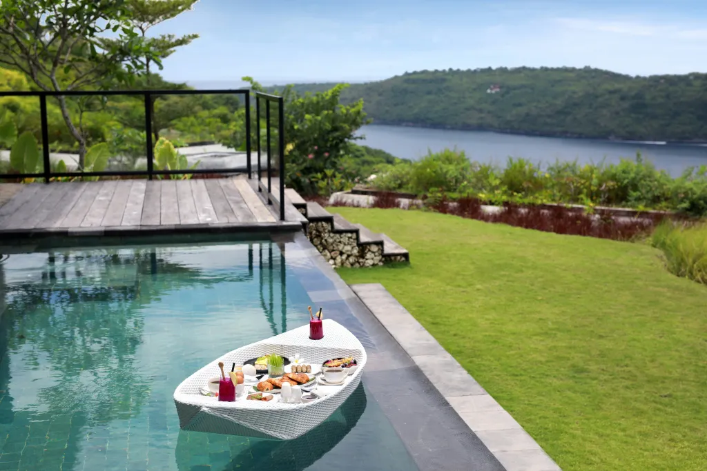 Une table décorée de plats et de boissons flotte sur une piscine avec vue sur la mer.