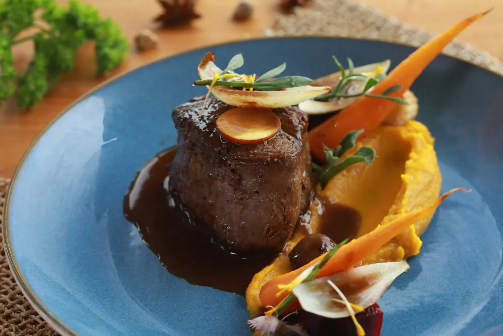 Assiette de viande accompagnée d'une sauce brune, de carottes et d'une purée.