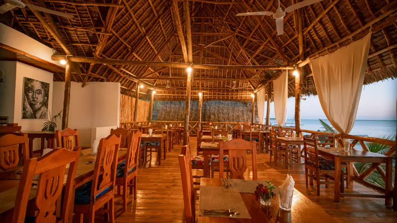 Une salle à manger ouverte sur l'océan, avec des tables en bois et des chaises.