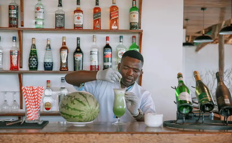 Un barman prépare une boisson fruitée derrière un comptoir bien garni.
