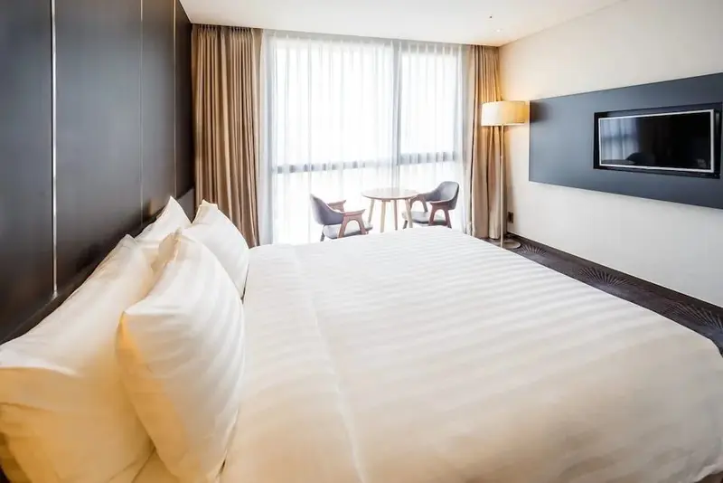 Une chambre lumineuse avec un grand lit et un coin salon près de la fenêtre.