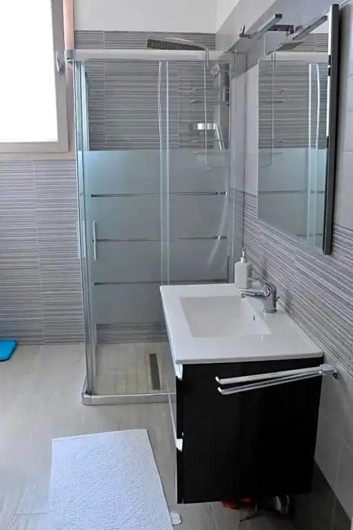 Une salle de bain moderne avec douche vitrée et vasque blanche.